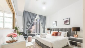 Ein modernes Schlafzimmer mit einem großen Bett, einem Glastisch, einem Stuhl und Blick auf die Stadt.