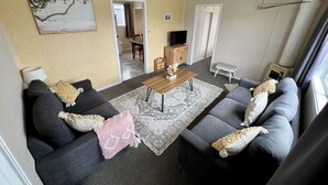 Un salon avec deux canapés, une table basse et un tapis. On aperçoit une télévision et un meuble en arrière-plan.