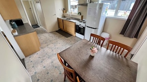 Une cuisine compacte comprenant une table à manger, des chaises en bois, un réfrigérateur, un four et une fenêtre donnant sur l’extérieur.