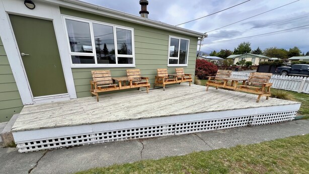 Une petite maison dotée d’un porche aménagé avec des chaises en bois et une petite table.