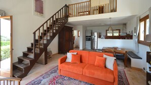 Un'ampia zona giorno con una scala in legno, un divano arancione vivace e una cucina sullo sfondo.