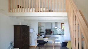 Un'ampia cucina con elettrodomestici moderni, una zona pranzo con tavolo e sedie, e una scala in legno che conduce a un piano superiore.