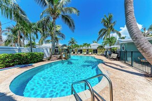 A pool area with clear blue water, surrounded by palm trees and lounge chairs.