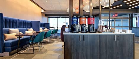 A modern hotel lobby with a seating area, a coffee bar, and a view of the outside.