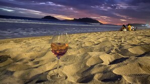 Ett glas vin på en sandstrand med en solnedgång i bakgrunden.