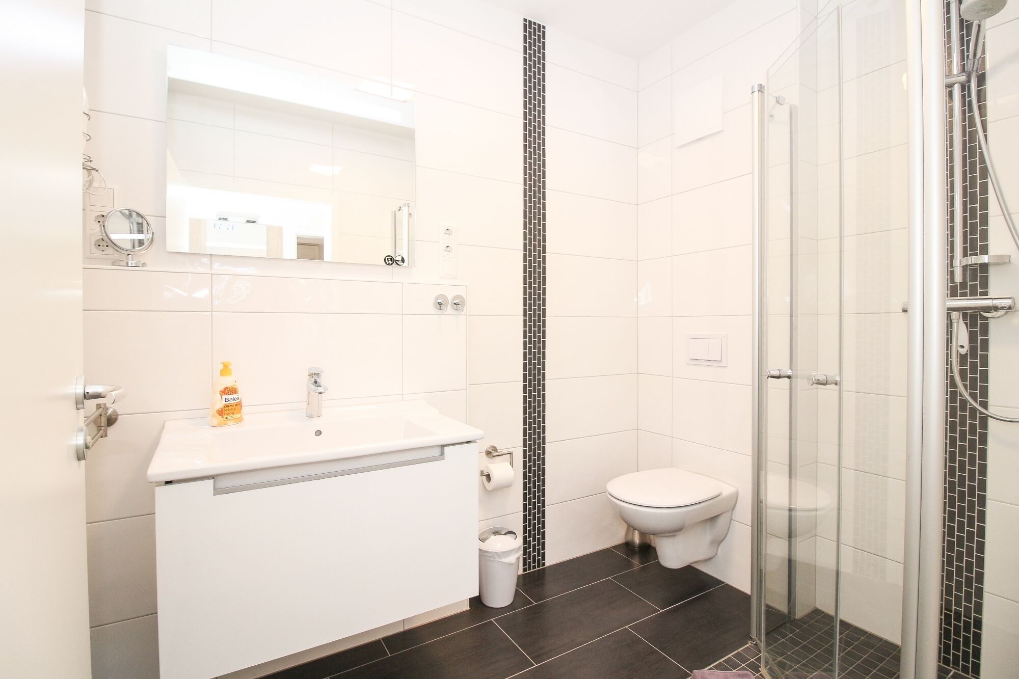 A modern bathroom with a white sink, toilet, and glass shower enclosure.
