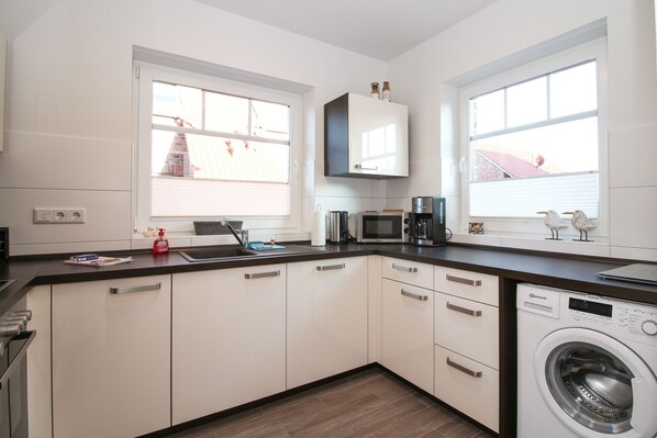 A modern kitchen with white cabinets, a built-in microwave, a coffee maker, and a washing machine.