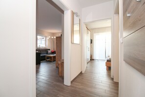 A hallway with wooden flooring, a sofa, a table, and a TV in the background.
