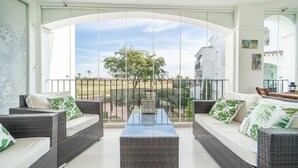 Een balkon met rieten meubels, een glazen tafel en uitzicht op een golfbaan.