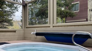 Un bain à remous sur une terrasse en bois, avec vue sur les arbres et une maison en arrière-plan.