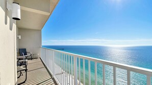 A balcony with a view of the ocean, a railing, and a chair.