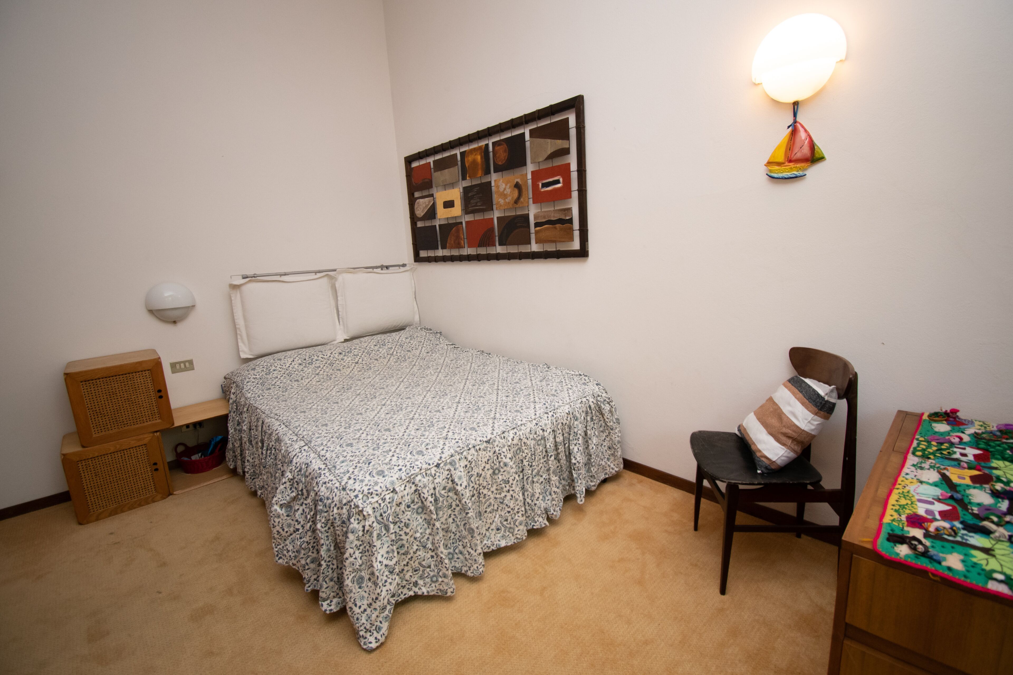 Een slaapkamer met een bed, een stoel, een tafel, een wandlamp en een lijst met een afbeelding.