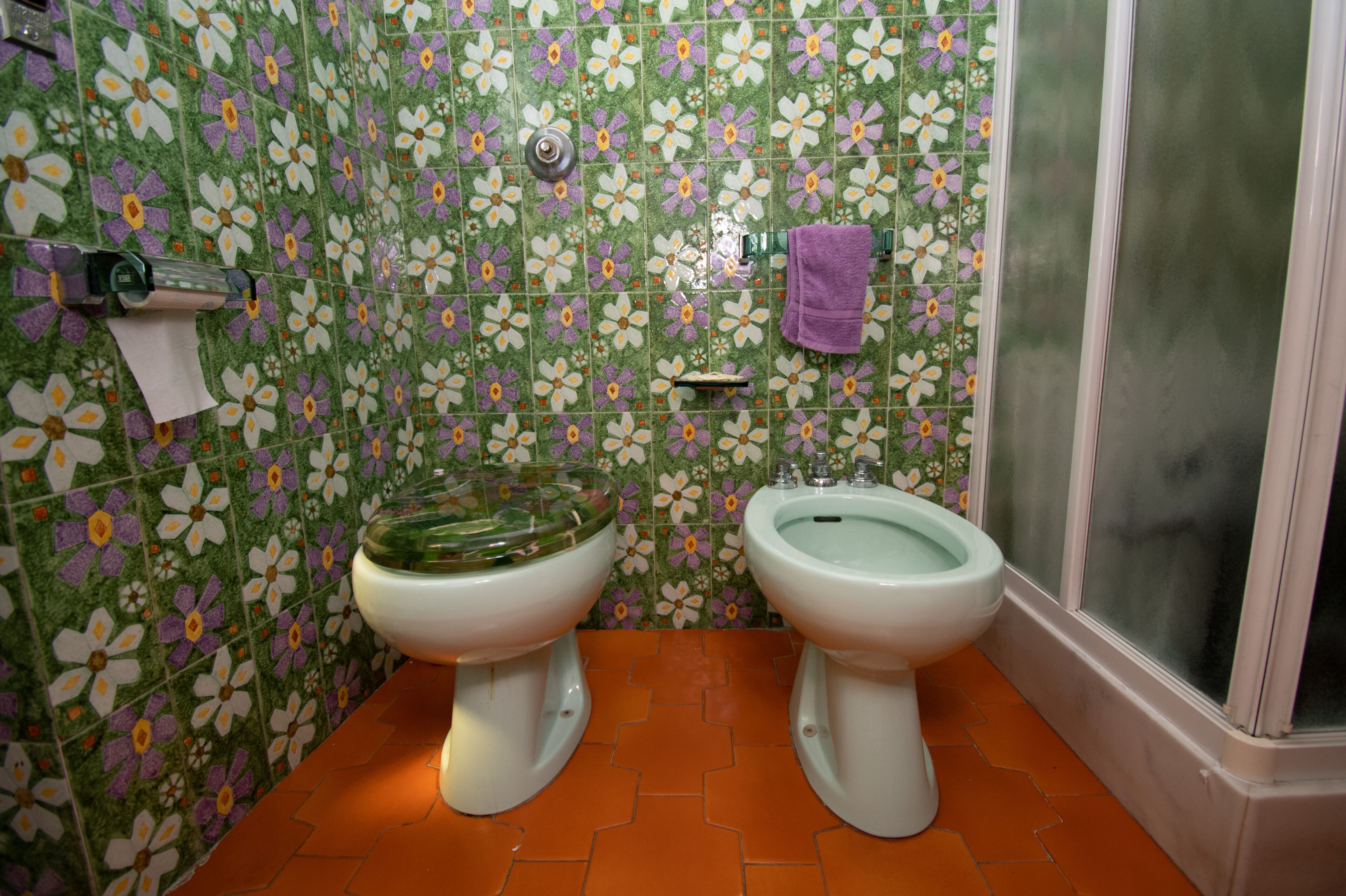 A bathroom with two toilets, a shower, and a tiled wall with a floral pattern.