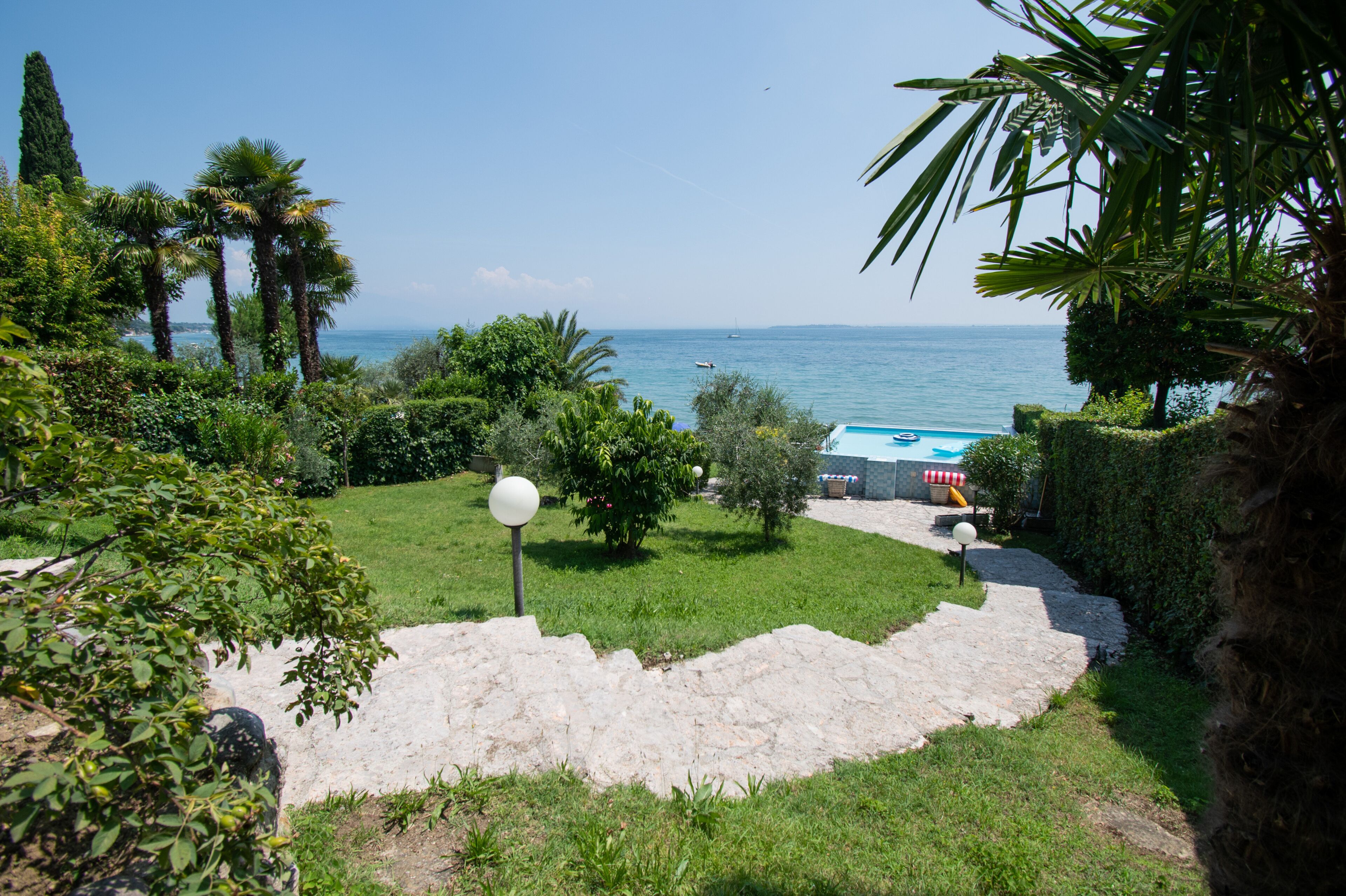 A garden with a stone pathway leading to a pool area, surrounded by lush greenery and palm trees.