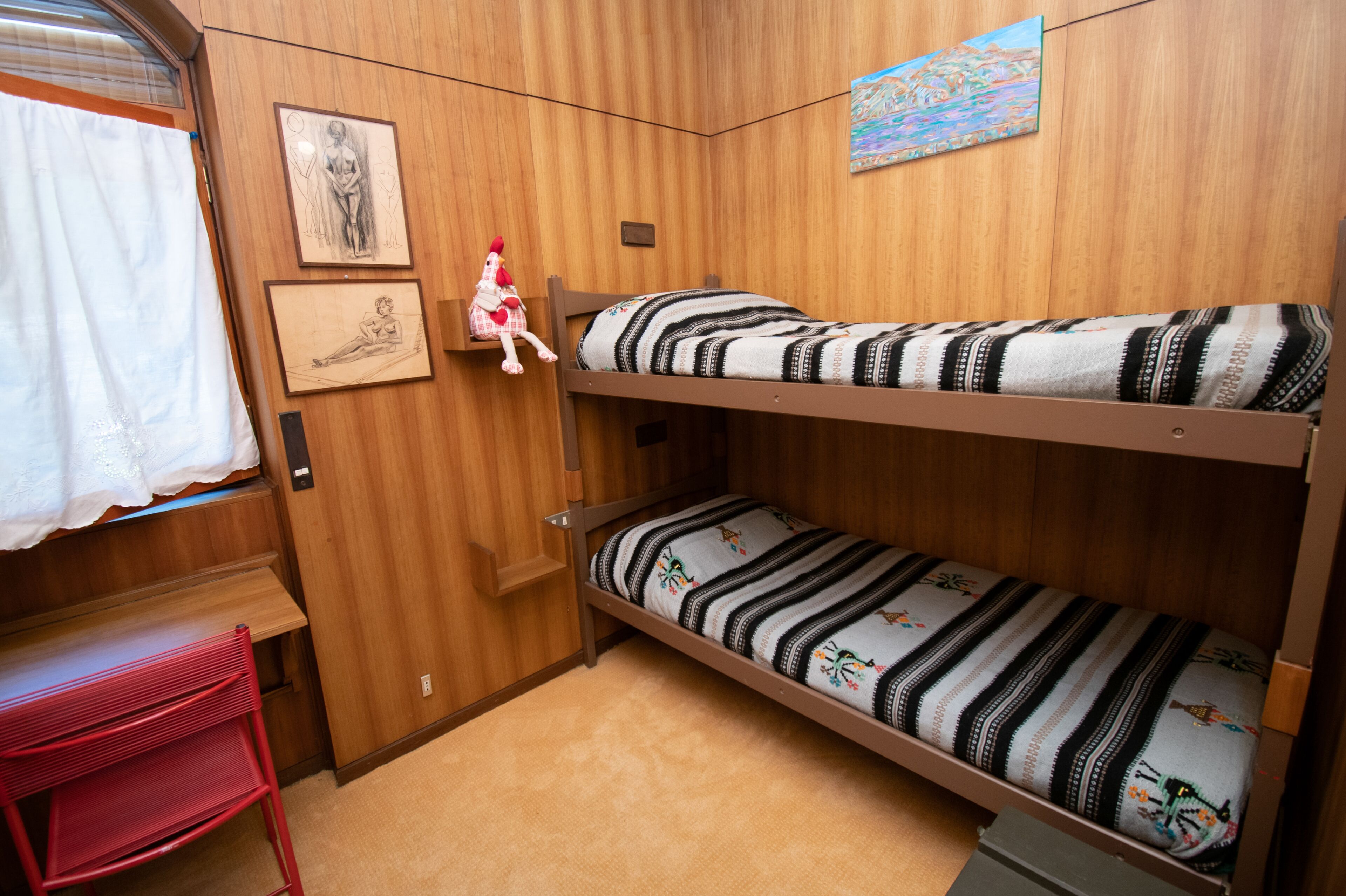 Dormitorio con literas, paredes de madera, un escritorio pequeño y una ventana con cortinas.