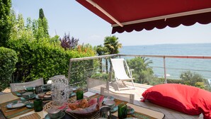 A terrace with a dining setup overlooking the sea, featuring a table with plates, cups, and a basket of food. - Villa Lydia (Padenghe sul Garda)