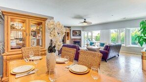 A dining area with a wooden table set for four, a wicker chair, and a large vase with white flowers.