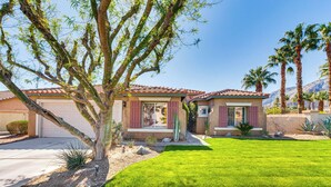 A two-story house with a red-tiled roof, a well-maintained lawn, and a variety of desert plants.