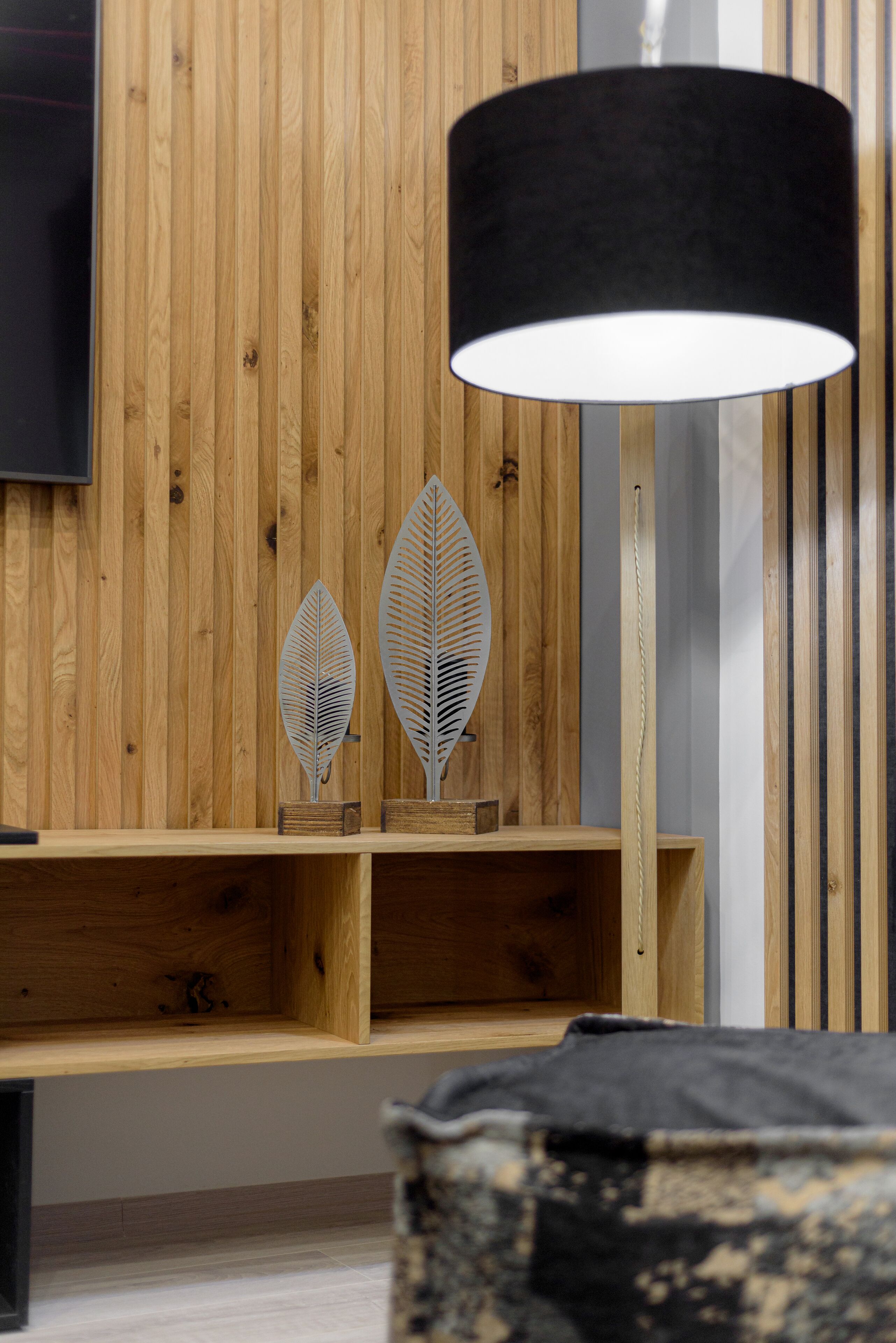 A wooden wall with a television mounted above a shelf holding decorative metal leaves.