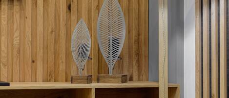 A wooden wall with a television mounted above a shelf holding decorative metal leaves.