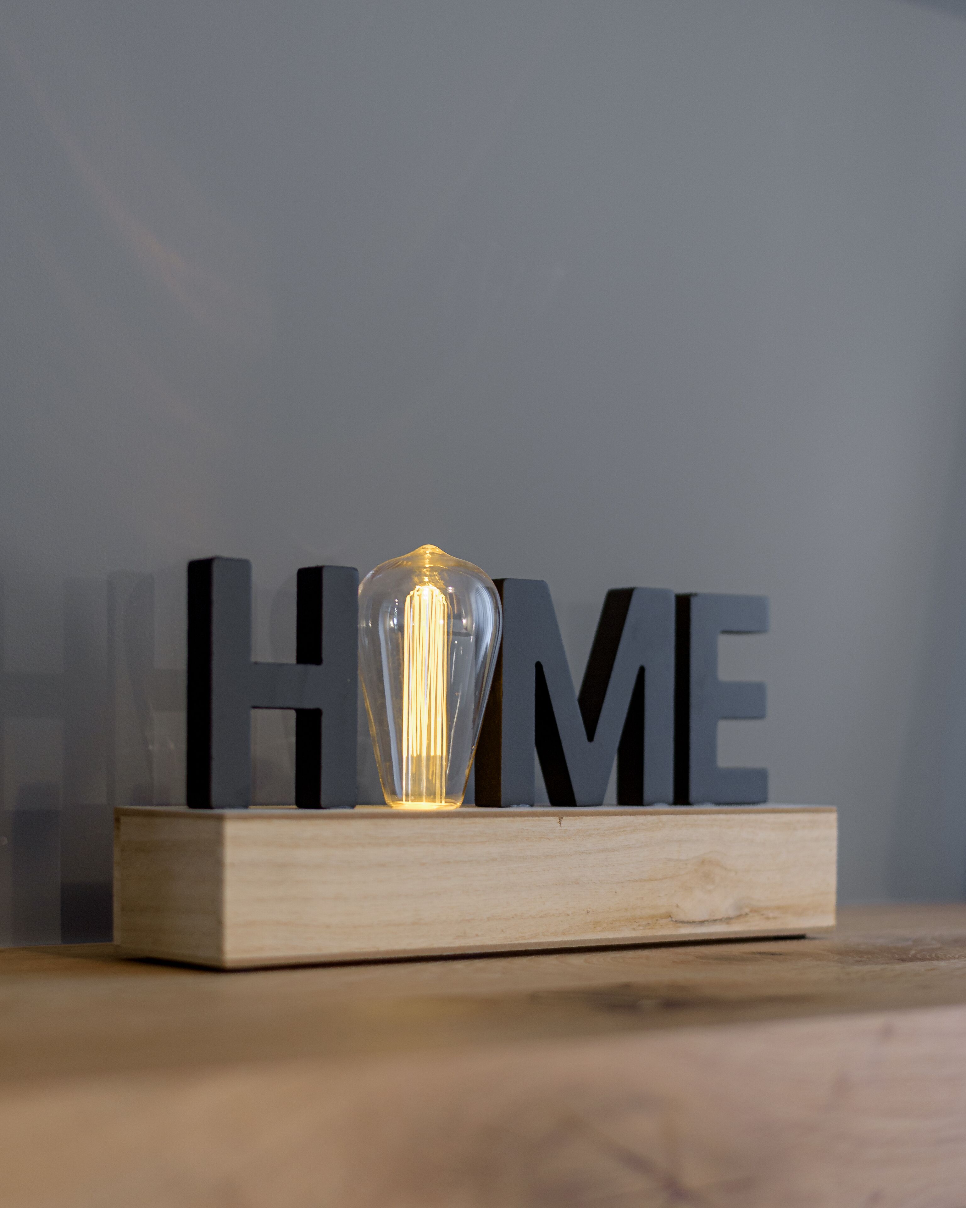 A clear glass light bulb on a wooden block with the letters "HOME" in black behind it.
