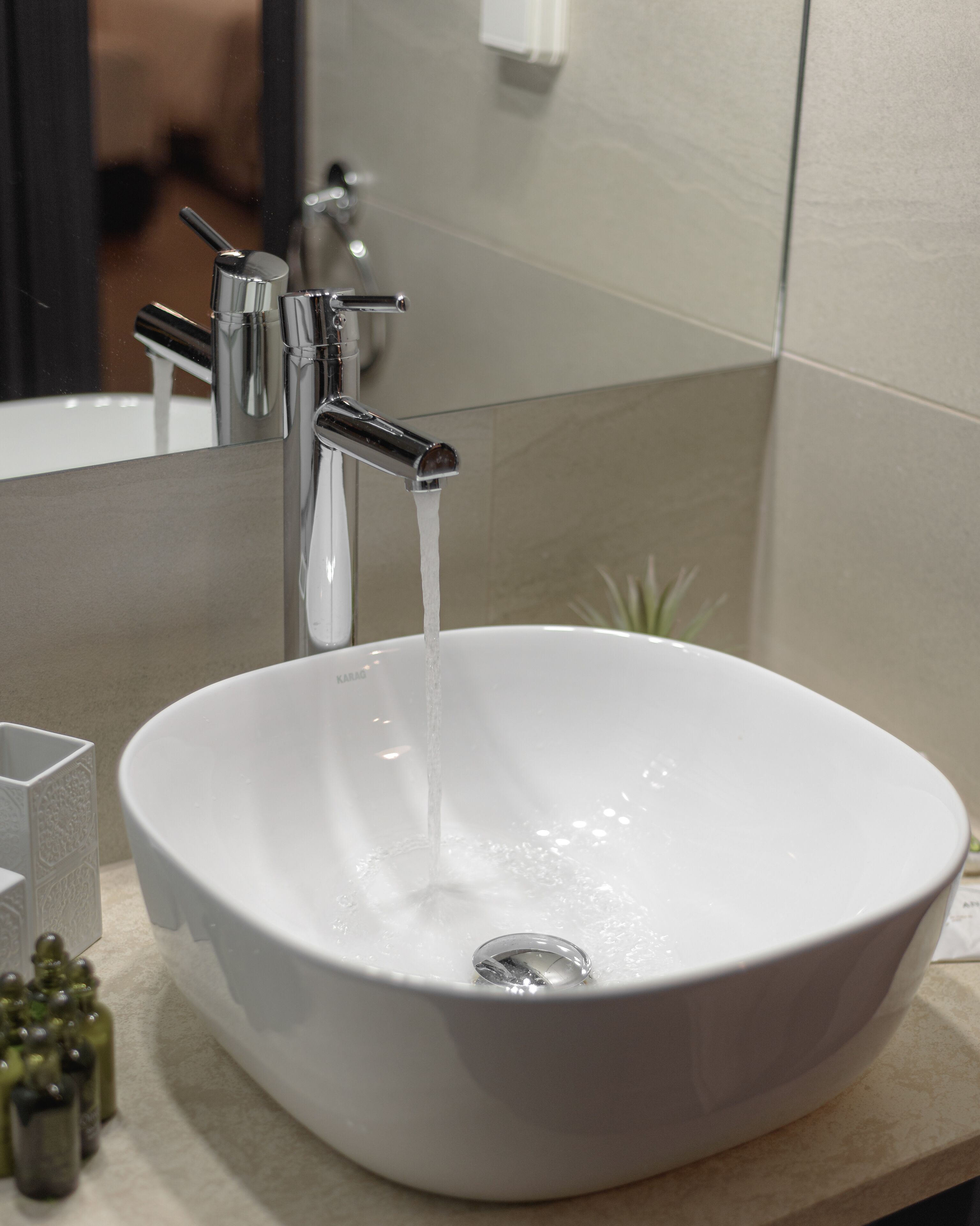 A white ceramic sink with a single faucet, a small potted plant, and a glass container on the countertop.