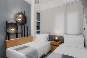 Two single beds with white linens and gray accents, accompanied by bedside tables and unique decorative panels.