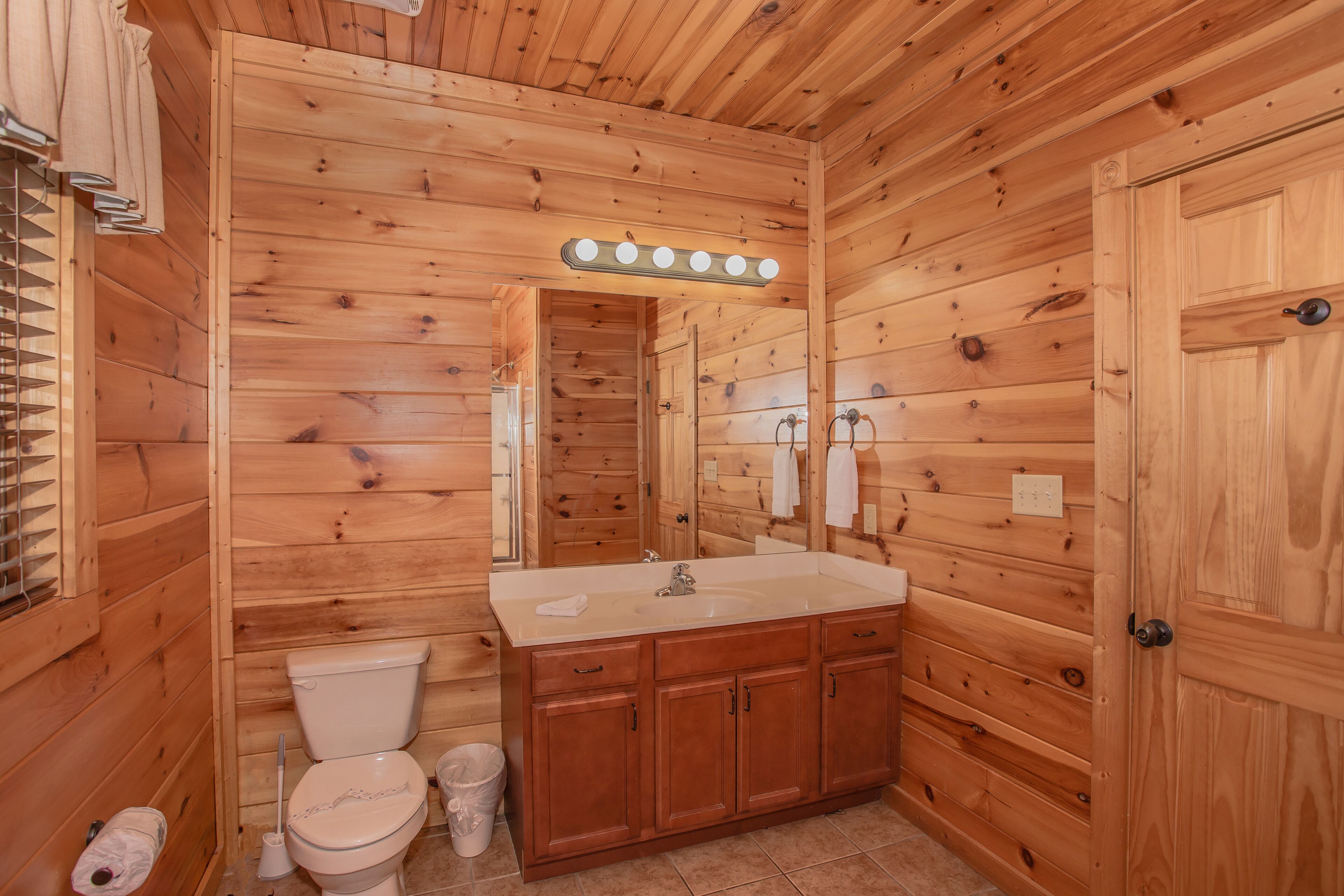 A wooden-paneled bathroom with a sink, mirror, and toilet.