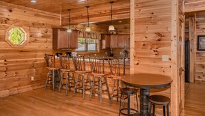 L’intérieur d’un chalet en bois comprend un coin bar, un plafond en bois et une grande fenêtre.