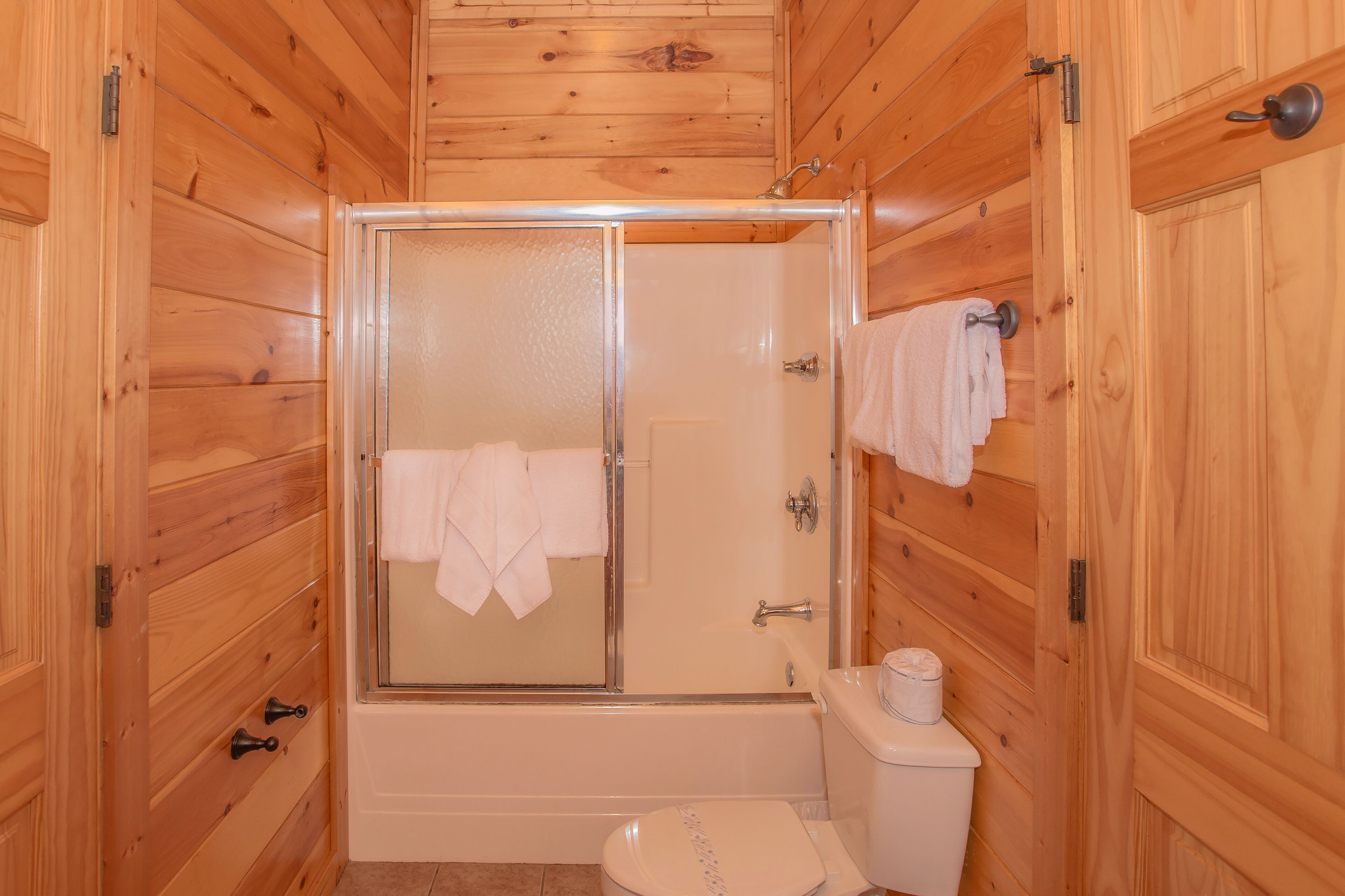 Ein Badezimmer mit Holzwänden, einer Dusche in Glaswand, einer Toilette und einer Badewanne.