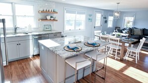 Een moderne keuken met een centraal eiland, witte kasten en een eethoek met witte stoelen.