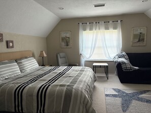A bedroom with a large bed, a chair, a small table, a couch, and a window with sheer curtains. - Private Suite (Wesley Chapel)