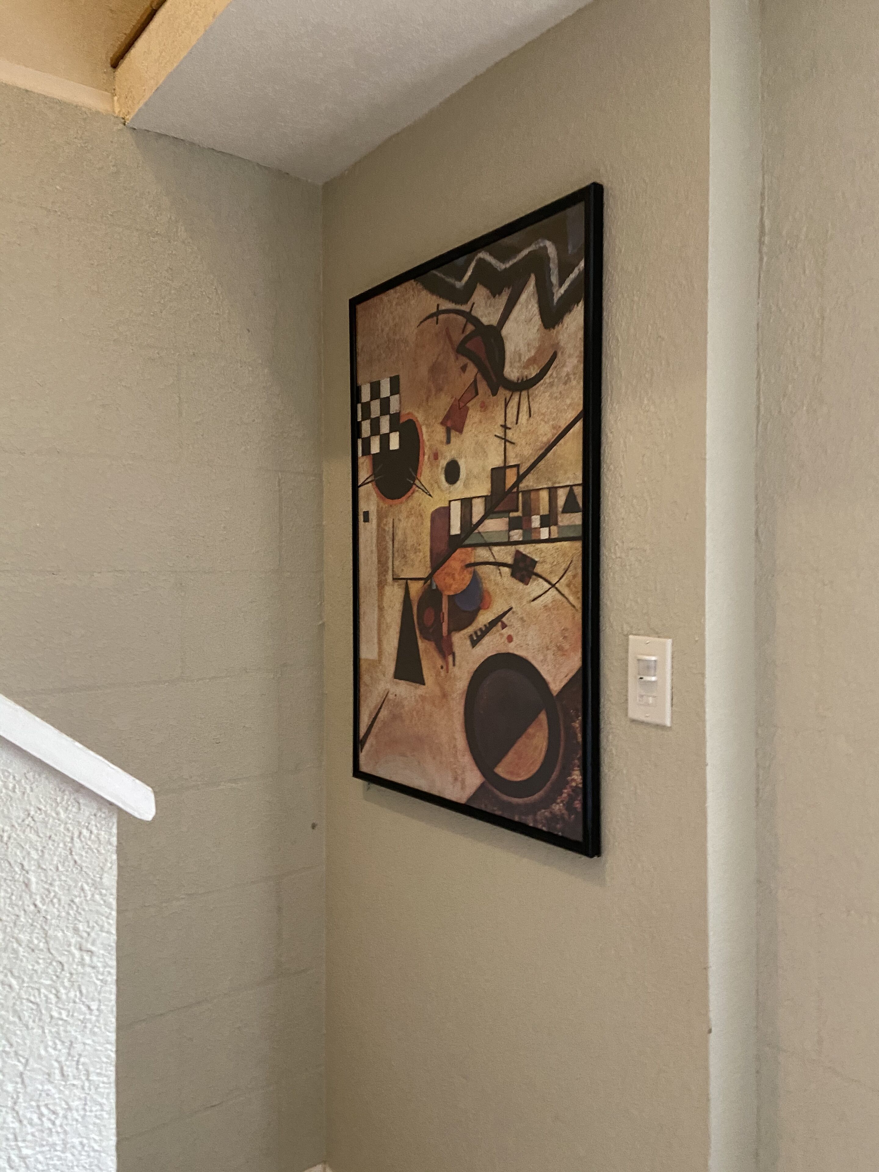 A room with a beige textured wall and a framed abstract painting.
