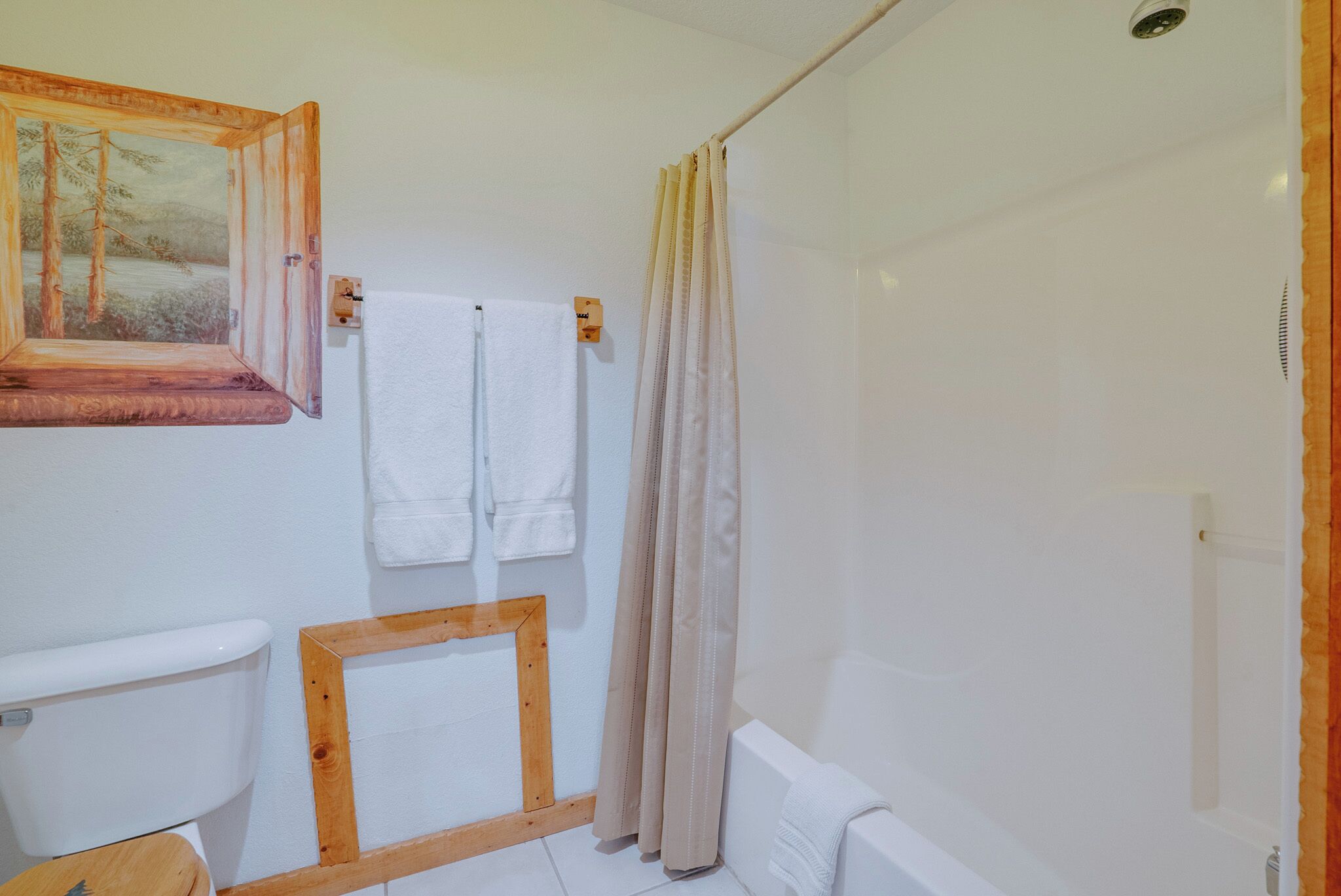 A bathroom with a wooden-framed window, white towels, a shower curtain, and a toilet.