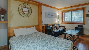 A bedroom with a bed, a sofa, a small table, a mirror, and a window with blinds.