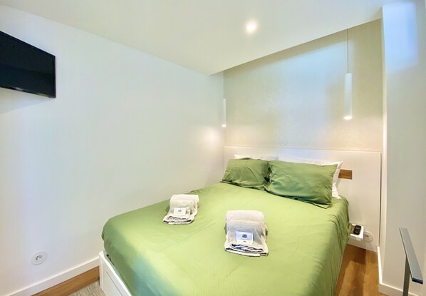 Una cama bien hecha con ropa de cama verde y dos toallas sobre ella.