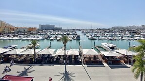 A marina with numerous boats docked, outdoor seating areas, and a large hotel building in the background.