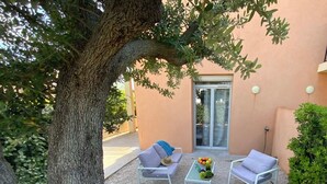 Une terrasse avec deux chaises et une table, entourée de gravier, avec un arbre et un bâtiment en arrière-plan.