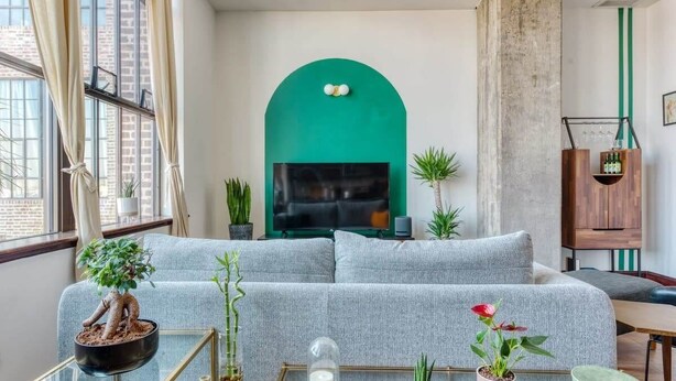 Ein modernes Wohnzimmer mit einem grauen Sofa, einem Glastisch und Blumentöpfen.