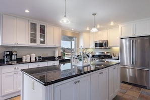 A modern kitchen with white cabinets, a central island, stainless steel appliances, and pendant lighting.