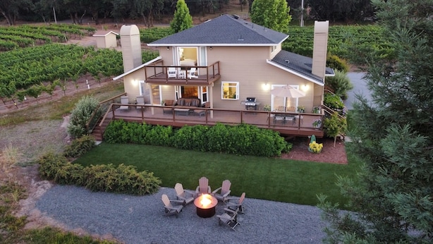 A two-story house with a deck, outdoor seating area, and a fire pit.