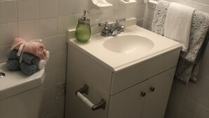 Un baño con inodoro, lavamanos y espejo. Hay toallas sobre el inodoro y un dispensador de jabón en el lavamanos.