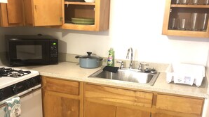 Una cocina con armarios de madera, microondas, estufa, lavaplatos y escurreplatos.