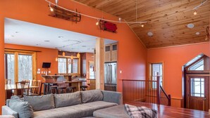 A spacious living room with a gray sectional sofa, a wooden coffee table, and a patterned rug. - Maine Stay- Contemporary Mountain Home, Spectaular Outdoor Space! (Newry)