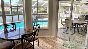 Un espace repas avec vue sur une piscine, grâce à de grandes fenêtres.
