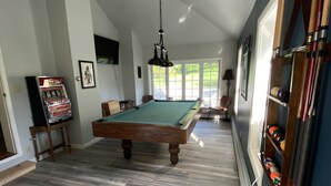 Een pooltafel in een ruimte met houten vloer, een plafondventilator en een biljarthouder.