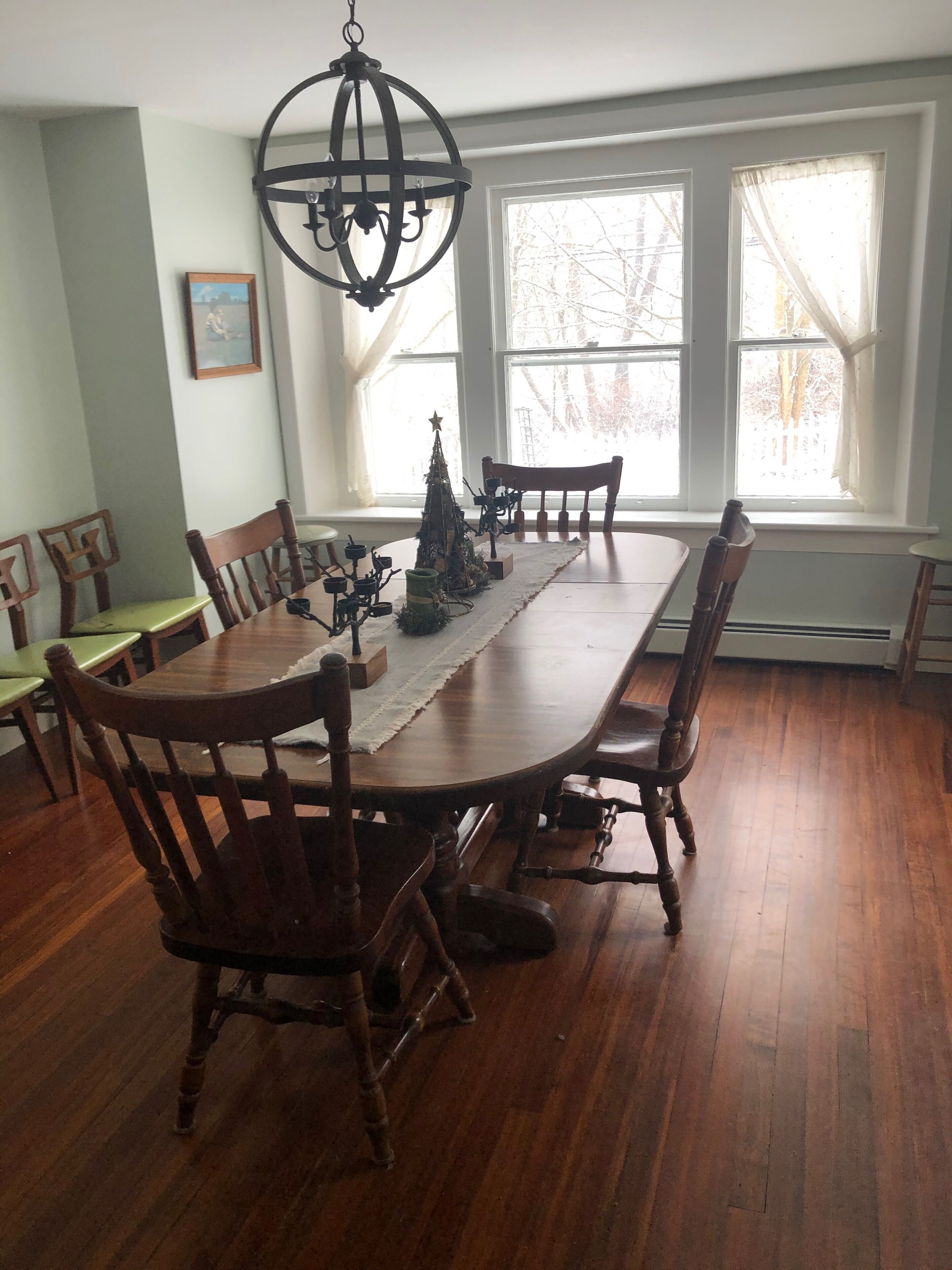 Un comedor con una mesa de madera, sillas, una araña y un pequeño árbol de Navidad.