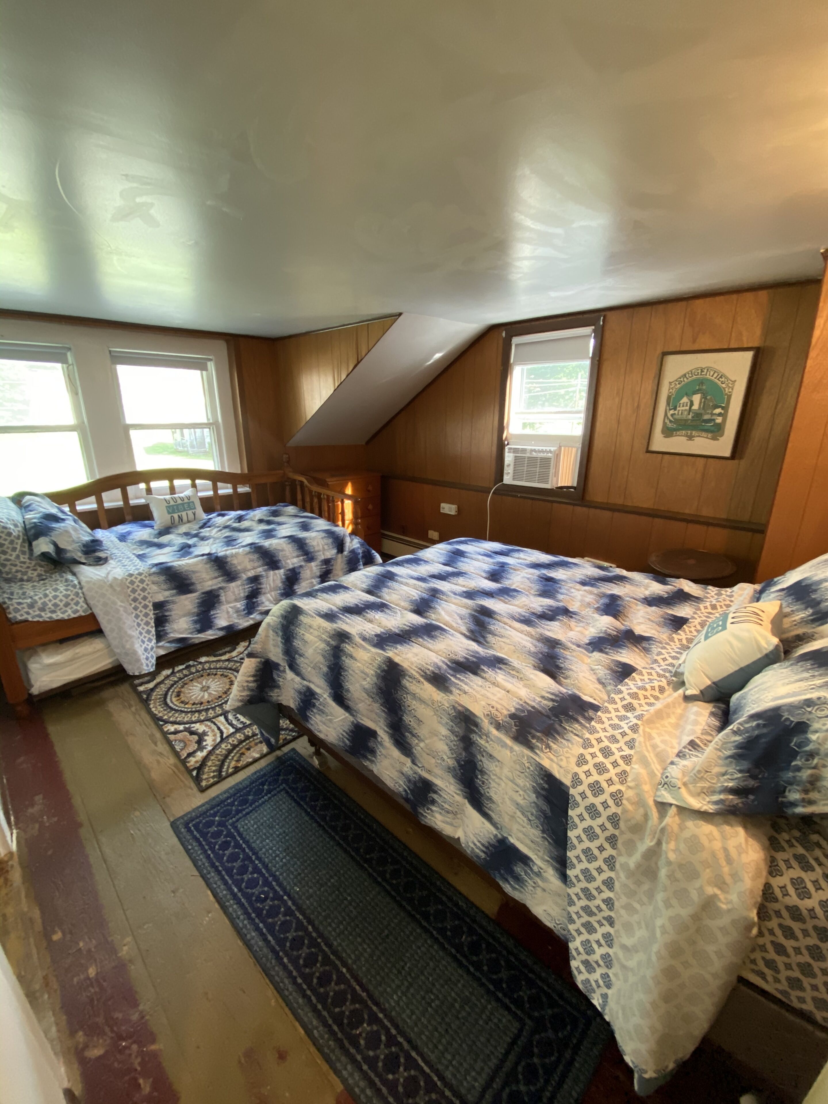 A bedroom with two beds, wooden walls, a sloped ceiling, and a window with a view.
