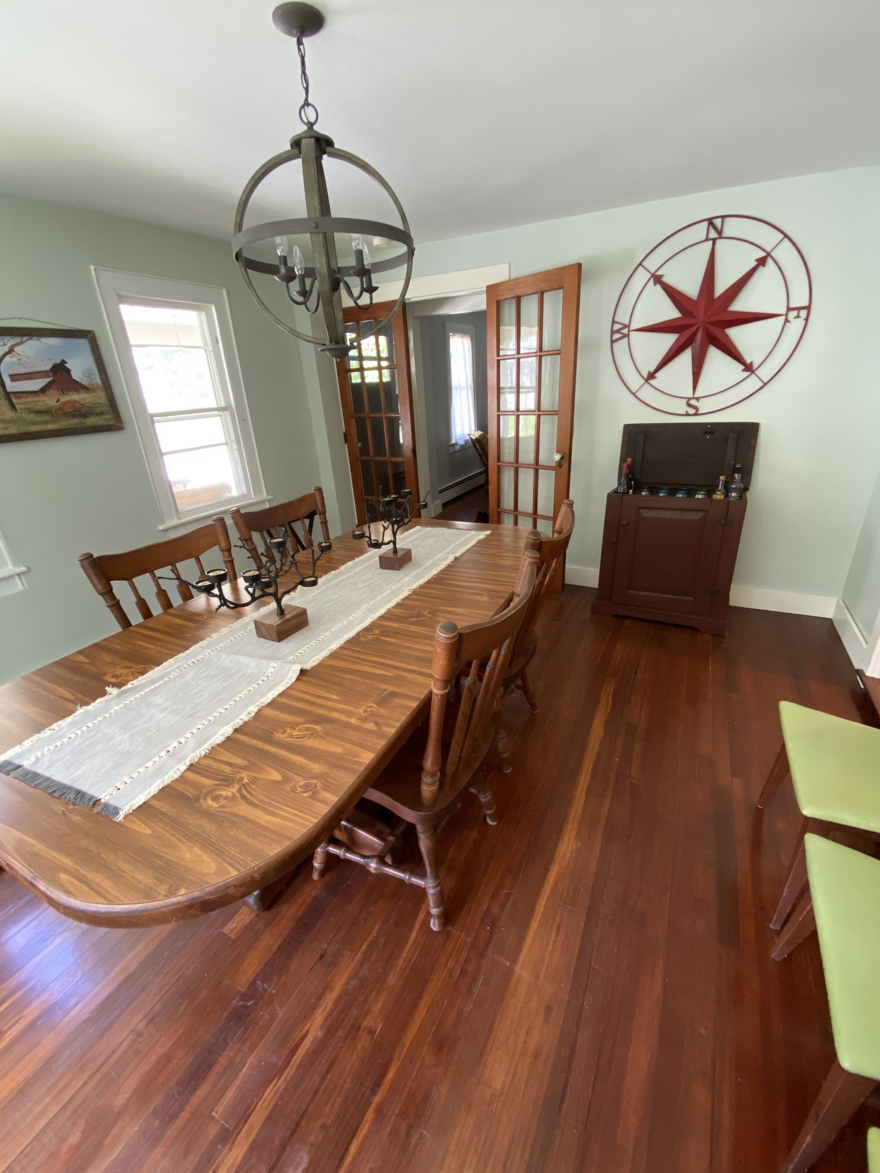 Une salle à manger avec une table en bois, des chaises, un lustre et une décoration murale représentant une boussole.