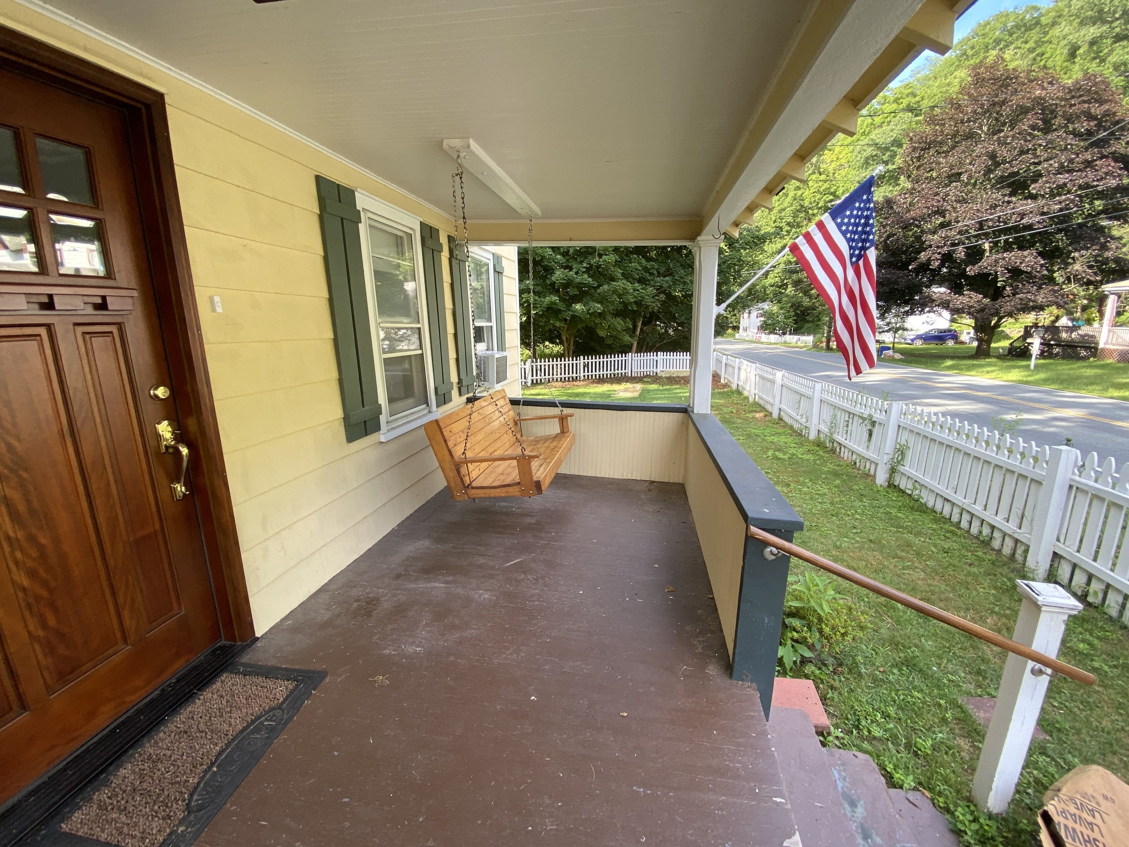 Un portico con un'altalena in legno, una recinzione di legno bianco e una bandiera americana.